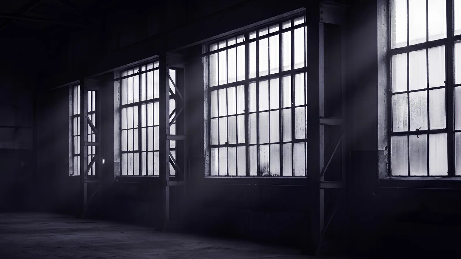 A dark industrial interior with tall windows